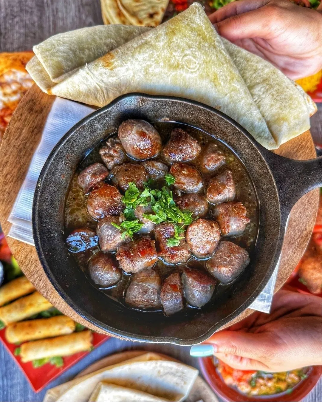 Sizzling browned sausage pieces in a skillet with pita and mezze plates